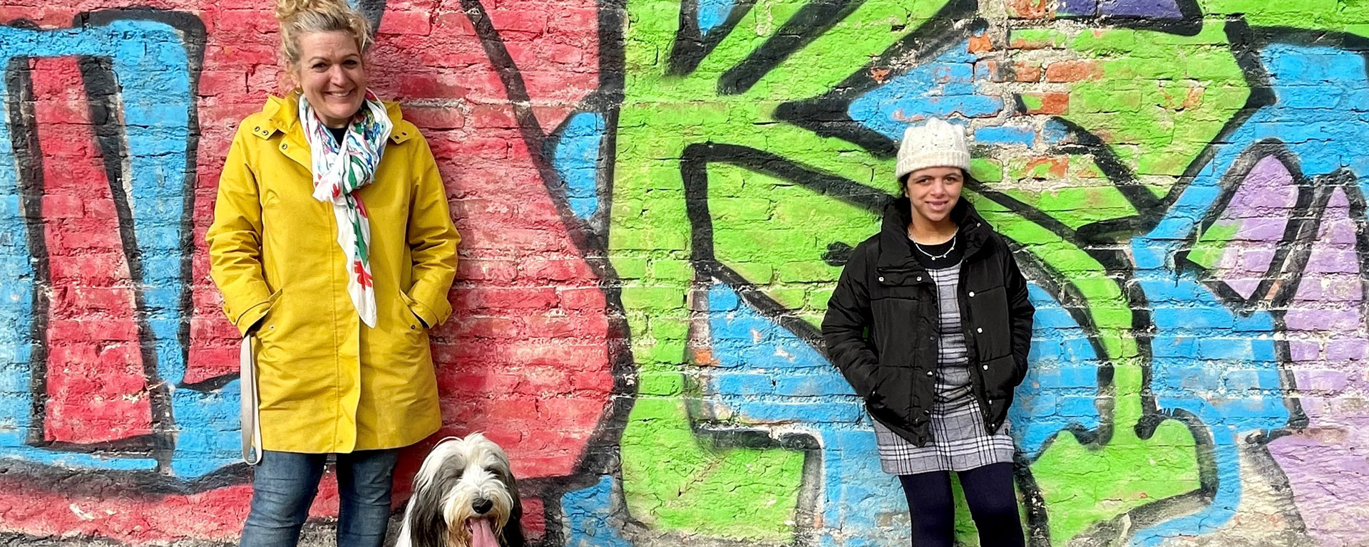 Eine Schülerin der Otto-Steiner-Schule steht zusammen mit einer Lehrerin und dem Schulhund vor einer Graffitiwand