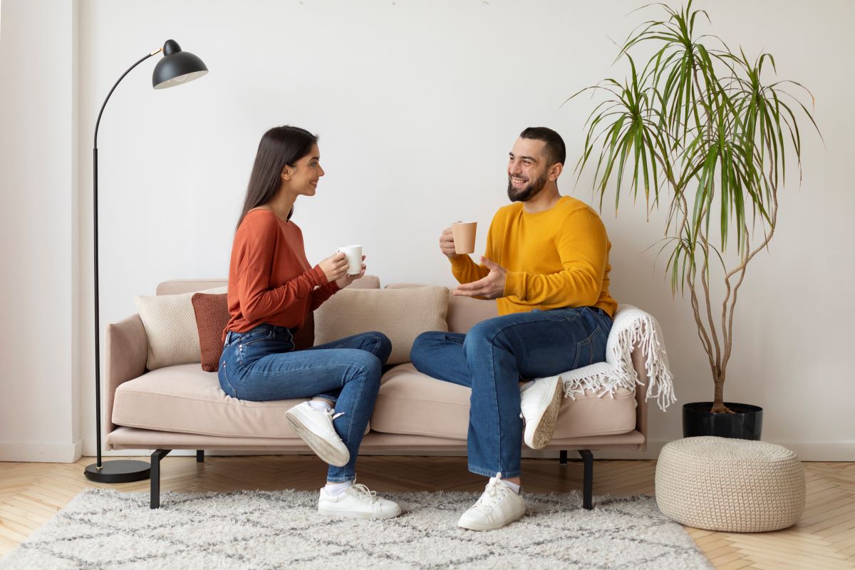 Frau und Mann sitzen auf Sofa und lächeln sich an mit einer Tasse in der Hand