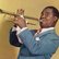 Trompete spielender Louis Armstrong, welcher einen Anzug trägt.