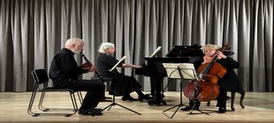 Drei Musiker*innen auf einer Bühne mit Flügel, Cello und Klarinette