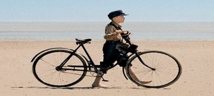 Junge schiebt Fahrrad am Strand