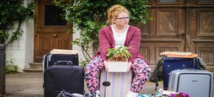 Kirsten Lange sitzt mit gepackten Koffern vor einer Türe