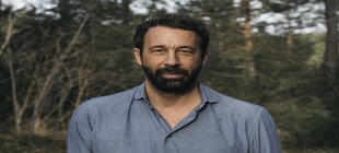 Portraitaufnahme eines schwarzhaarigen Mannes mit Bart und Bäumen im Hintergrund