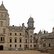 Historisches Schloss aus hellem Naturstein mit mehreren Türmen, einem Uhrturm und großem Innenhof.