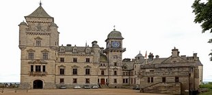 Historisches Schloss aus hellem Naturstein mit mehreren Türmen, einem Uhrturm und großem Innenhof.
