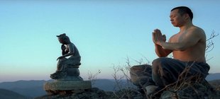 Meditierender Mönch neben buddhistischer Statue