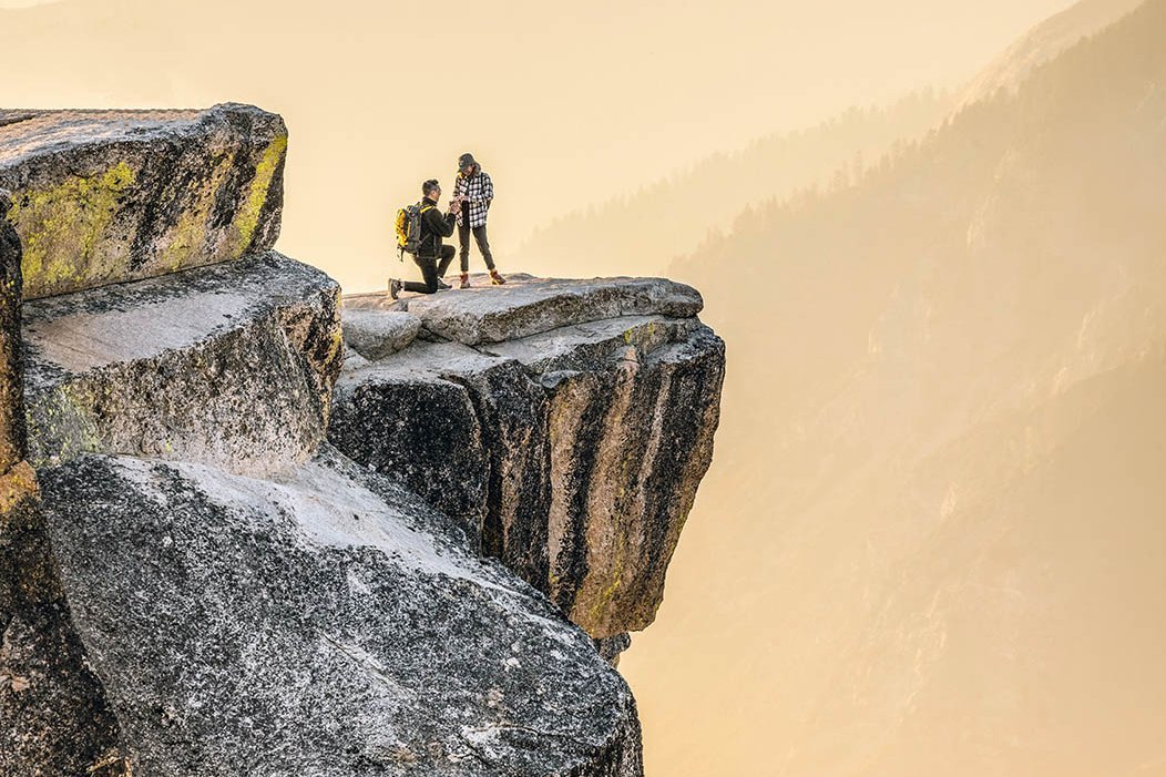 Mann macht Frau auf einem Felsen über einem Abgrund einen Heiratsantrag