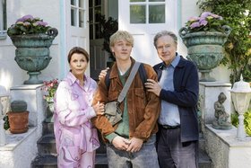 Großeltern und der erwachsene Enkel stehen vor einer pompösen Haustüre