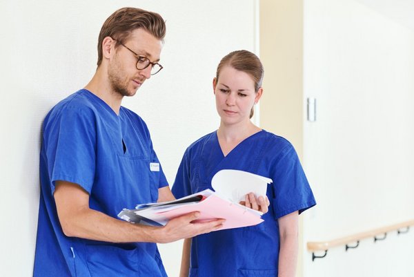 Zwei junge Ärzte stehen nebeneinander uns schauen auf eine Patientenakte