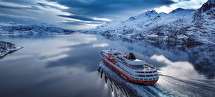 Hurtigruten-Postschiff mit schneebedeckten Bergen im Hintergrund
