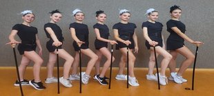 7 Mädchen in Gymnastikanzug mit Stock