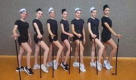 7 Mädchen in Gymnastikanzug mit Stock