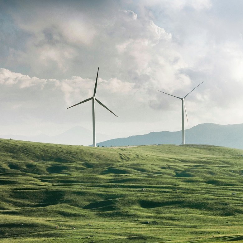 Zwei Windräder vor einer hügeligen Wiesenlandschaft.