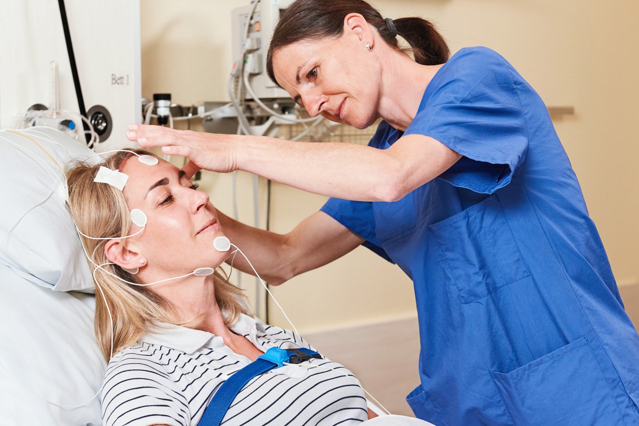 Einer Patientin werden von einer Pflegekraft Elektroden am Kopf angebracht.