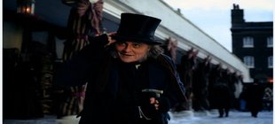 Person in historischer Kleidung mit Zylinderhut und Gehstock steht in einer verschneiten Straße des 19. Jahrhunderts vor einer Ladenzeile.