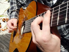 im Ausschnitt des Fotos sind zwei Hände zu sehen, die eine Gitarre halten und spielen