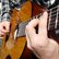 im Ausschnitt des Fotos sind zwei Hände zu sehen, die eine Gitarre halten und spielen