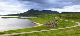 Meeresbucht mit Berg im Hintergrund und der Ruine einer Steinhütte im Vordergrund