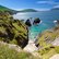 Grün bewachsene Steilküste im Sonnenschein darunter blaues Meer