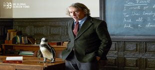 Ein mittelalter Mann, neben ihm sitzt ein Pinguin auf dem Tisch