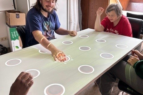 Tisch mit Muster und Menschen auf Stühlen, die miteinander ein Gesellschaftsspiel spielen