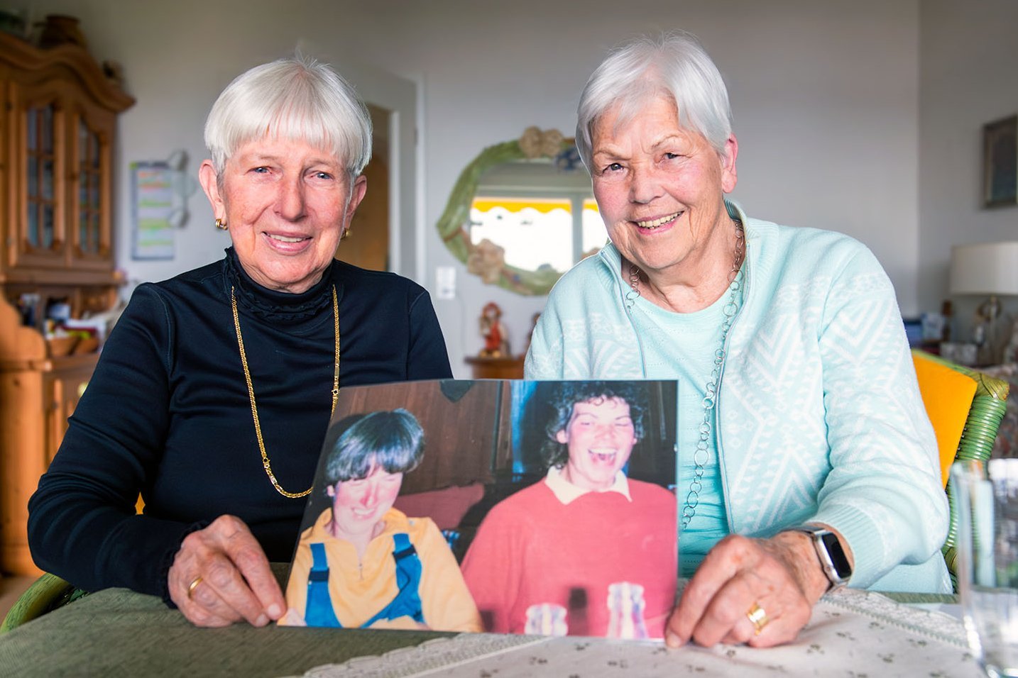 Zwei Seniorinnen halten ein Foto von sich aus jüngeren Jahren in die Kamera