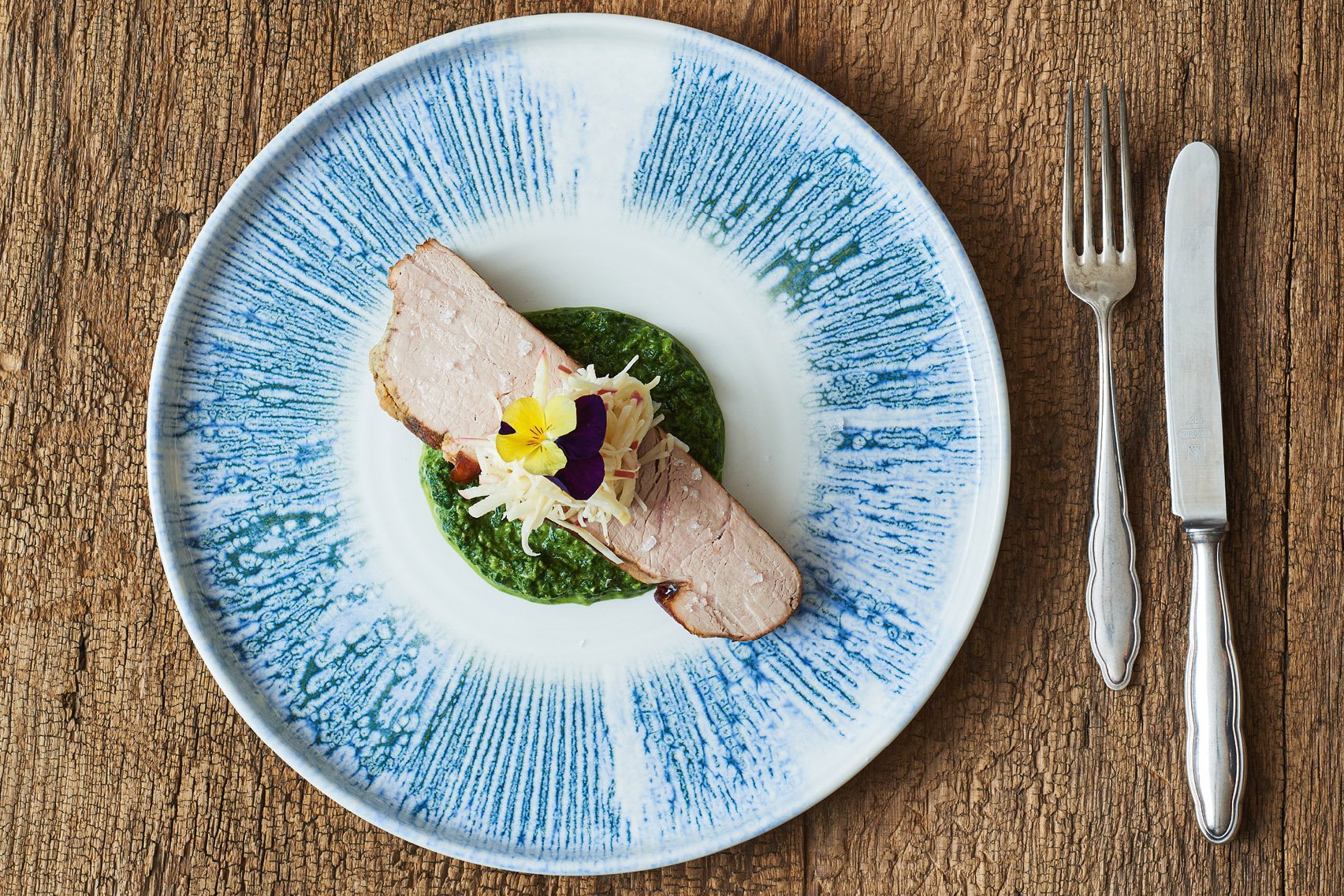 Ein weiß-blauer Teller mit Shabby-Chic Besteck auf einem Holztisch. Darauf angerichtet ein Stück Tafelspitz mit Beilagen