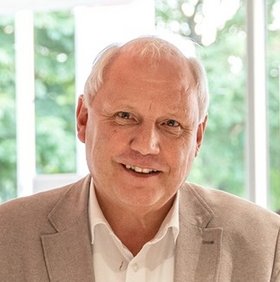 Mann in hellem Anzug vor einem grünen Hintergrund