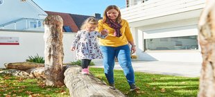 Frau mit Kind an der Hand, das über einen Baumstamm balanciert