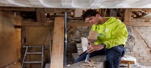 Ein junger Mann bearbeitet einen Holzbalken