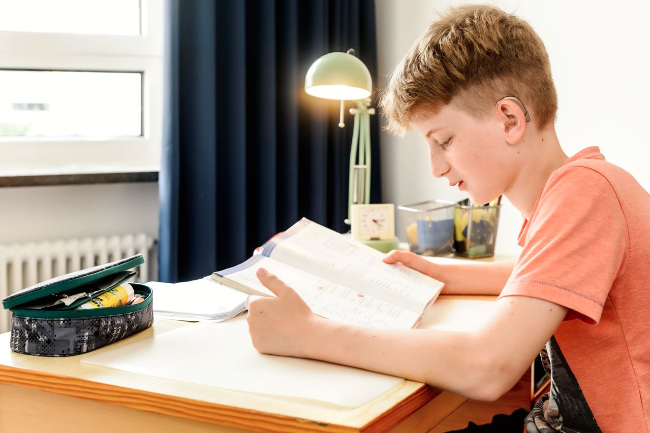 Ein Junge sitzt an seinem Schreibtisch und liest 