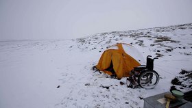 Gelbes Zelt in einer verschneiten Landschaft neben einem leeren Rollstuhl