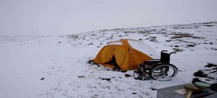 Gelbes Zelt in einer verschneiten Landschaft neben einem leeren Rollstuhl