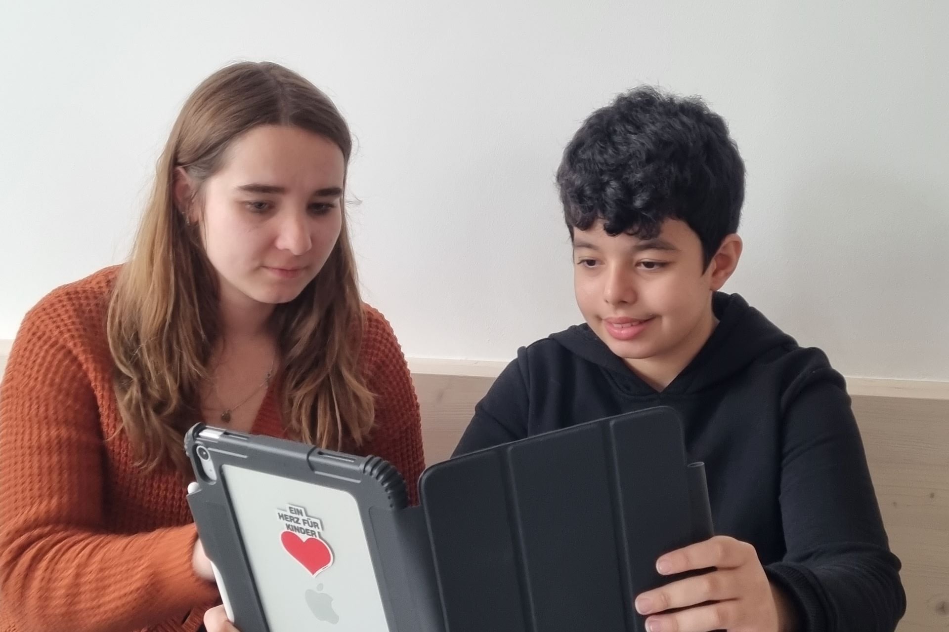 Eine Junge und eine Mitarbeiterin der Augustinum Tagesstätte schauen gemeinsam in ein iPad