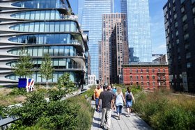 Menschen spazieren auf einem begrünten Fußweg zwischen modernen Hochhäusern und historischen Backsteingebäuden in im dicht bebauten New York.