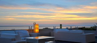 Terrassenmöbel und Stehleuchte vor Wasserlandschaft bei Sonnenuntergang