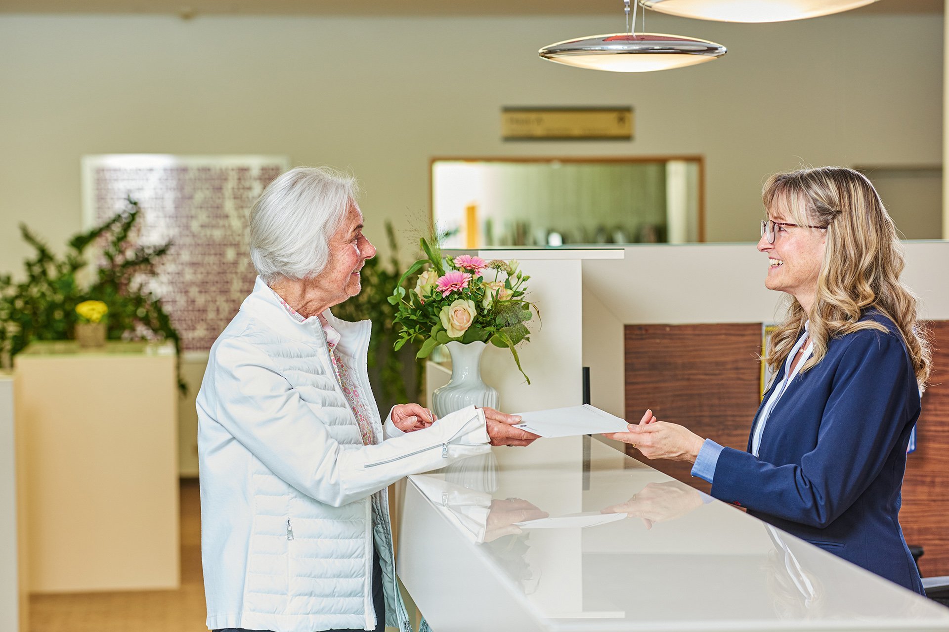 Eine Mitarbeiterin des Empfangs übergibt einen Brief an eine Seniorin 