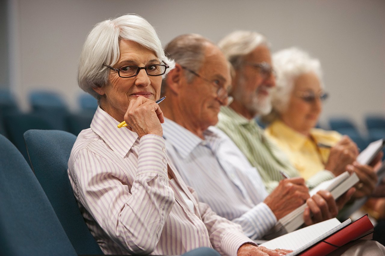 Vier Senior*innen sitzen mit Stift und Papier in einem Saal