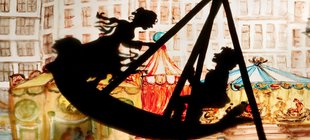 Vor einer beleuchteten Häuserkulisse ist der Schatten einer Schiffschaukle, besetzt mit zwei Personen zu sehen. 
