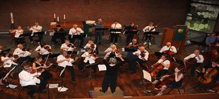 Musiker sitzen in Orchesteraufstellung vor einer Dirigentin