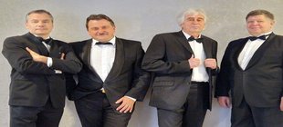 Vier Männer im schwarzen Anzug mit Fliege vor einer grauen Wand