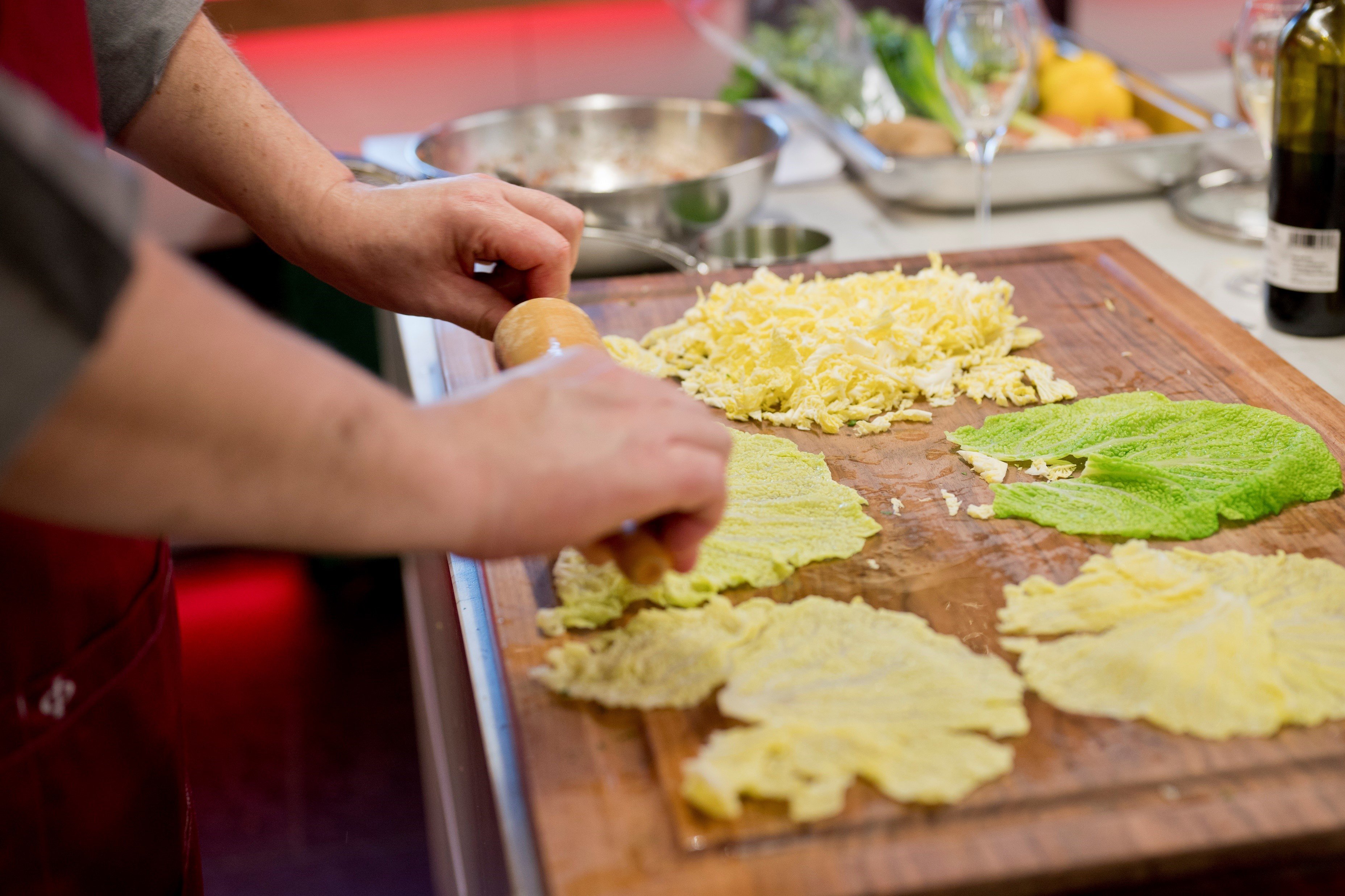 Ein Koch rollt gekochte Wirsingblätter für Rouladen auf, daneben liegen geschnittene Wirsingstreifen