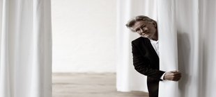 Ein Mann mit Brille im schwarzen Anzug vor einem weißen Hintergrund