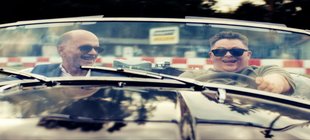 Hauptpersonen sitzen lachend im Auto 