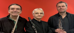 Drei schwarzgekleidete Männer mit Flöte, Oboe und Klarinette vor rotem Hintergrund