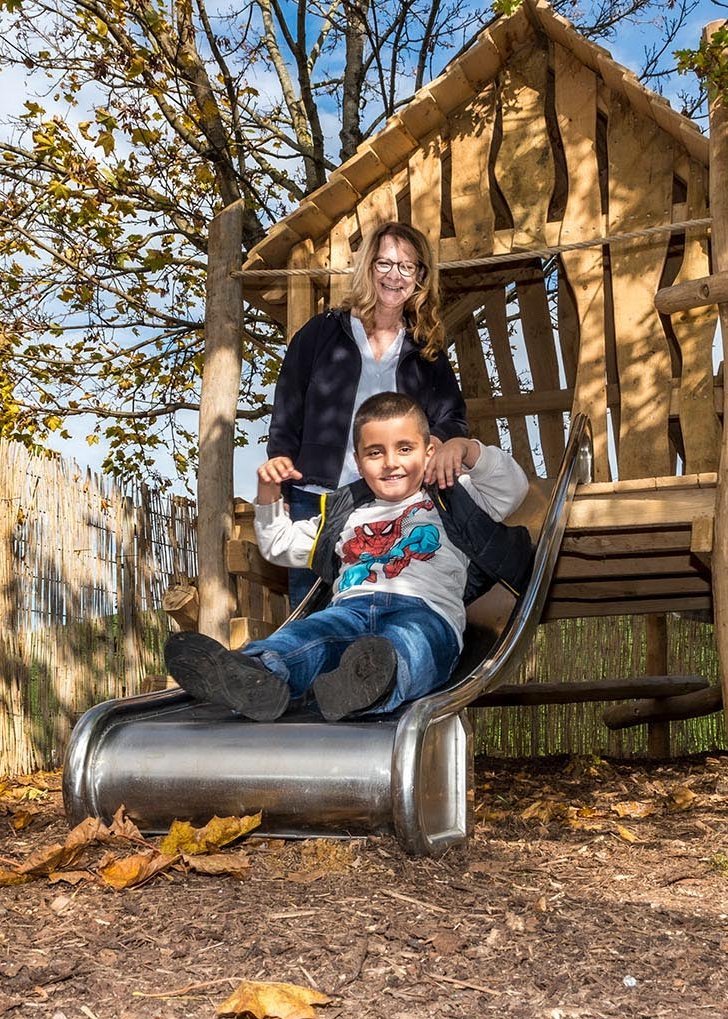 fröhlicher Junge auf einer Rutsche, im Hintergrund eine Erzieherin