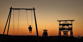 Kind auf einer Schaukel im Abendlicht mit Hochofen im Hintergrund