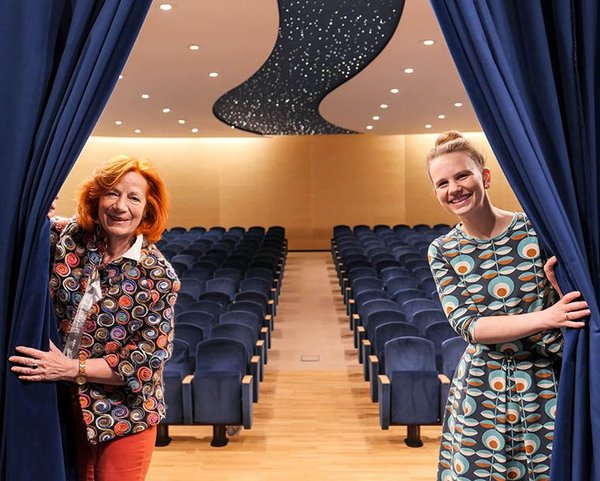 Zwei Kulturreferentinnen ziehen den Bühnenvorhang zur Seite; Theatersaal im Hintergrund