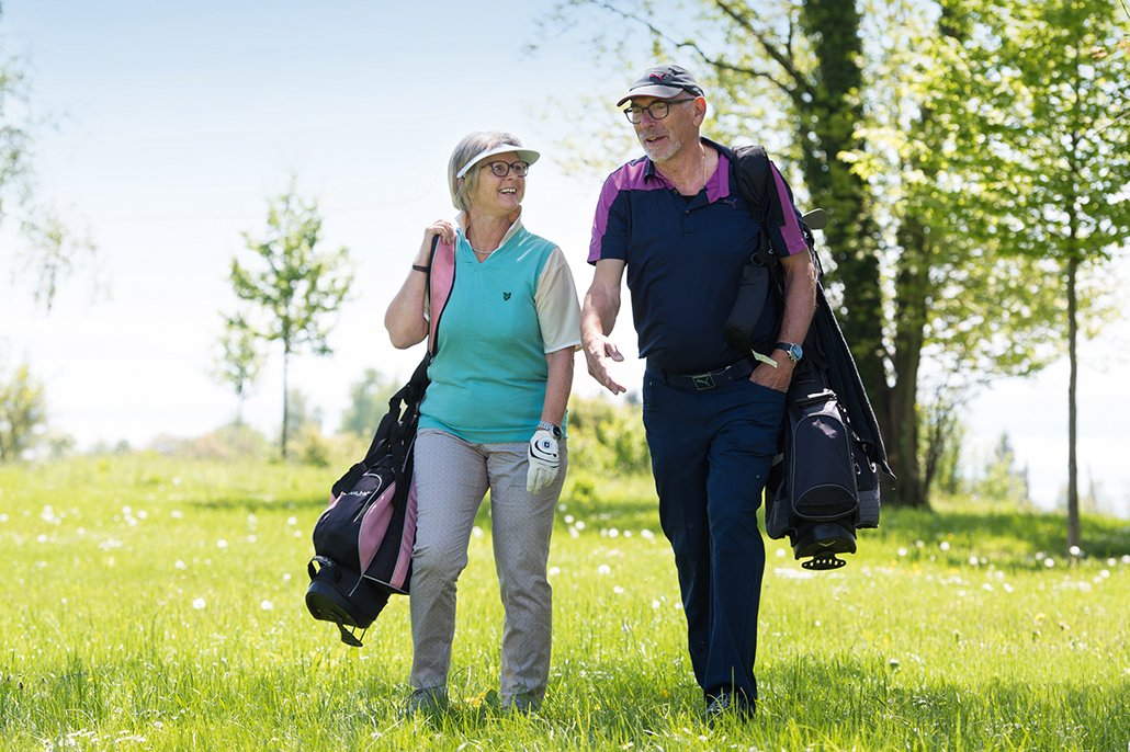 Mann und Frau mit geschulterten Golfbags