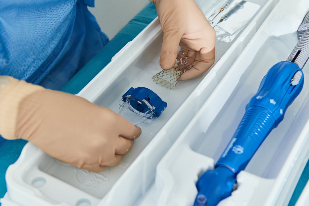 Zwei Hände fügen in einem sterilen Bad eine Aortenklappenprothese zusammen